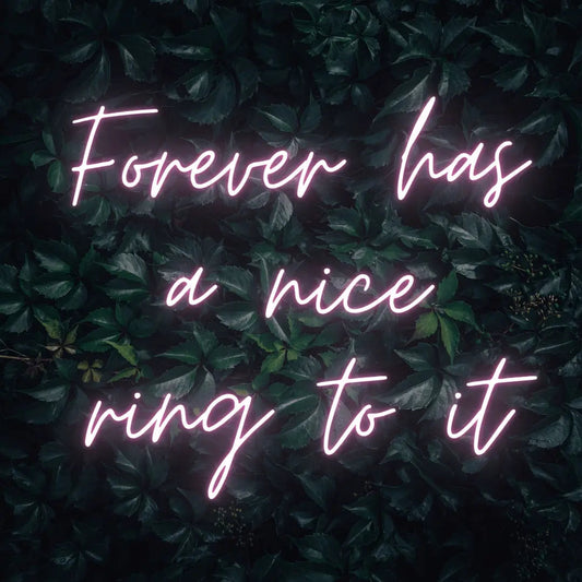 Forever Has a Nice Ring to It LED Neon Light Sign in pale pink, featuring three lines of script lettering against a dark foliage backdrop.