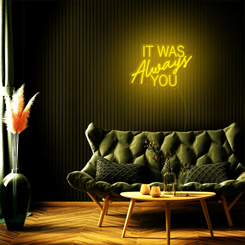 It Was Always You LED Neon Sign in yellow, featuring mixed script and block lettering above a dark tufted sofa.