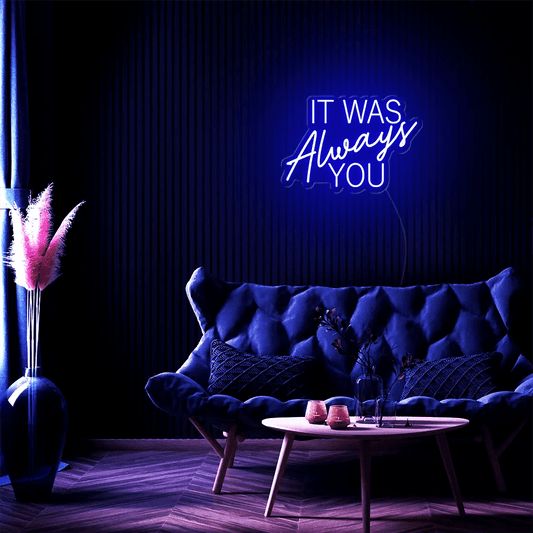 It Was Always You LED Neon Sign in blue, featuring mixed script and block lettering above a dark tufted sofa.