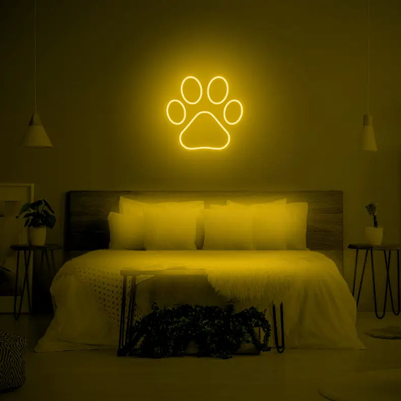 Paw LED Neon Light Sign in yellow, featuring paw-print outline illuminated above a bed.