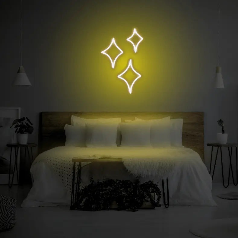 Sparkle LED Neon Light Sign in yellow, featuring three outlined sparkle shapes illuminated above a bed.