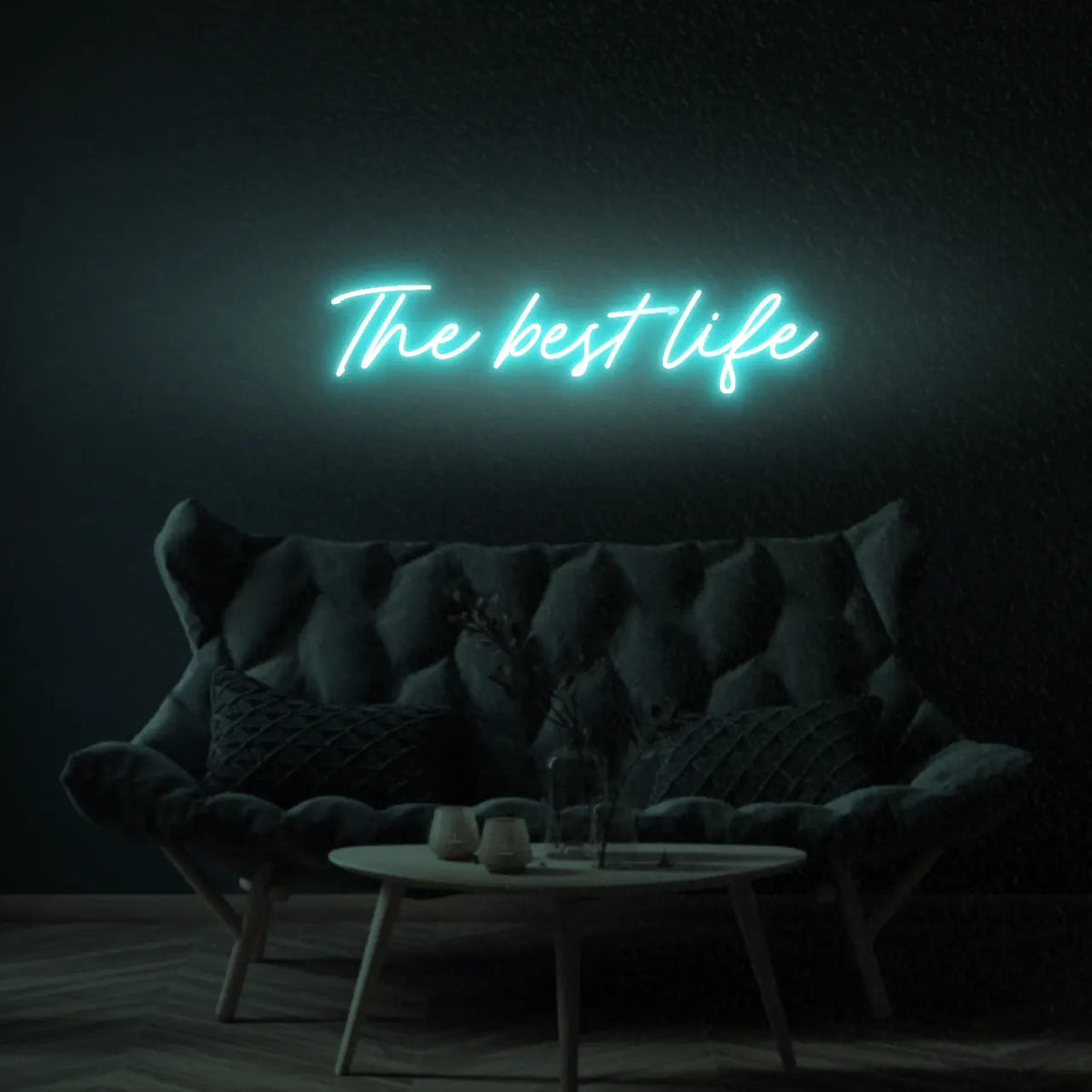 The Best Life LED Neon Light Sign in turquoise, featuring script lettering illuminated above a dark tufted sofa.