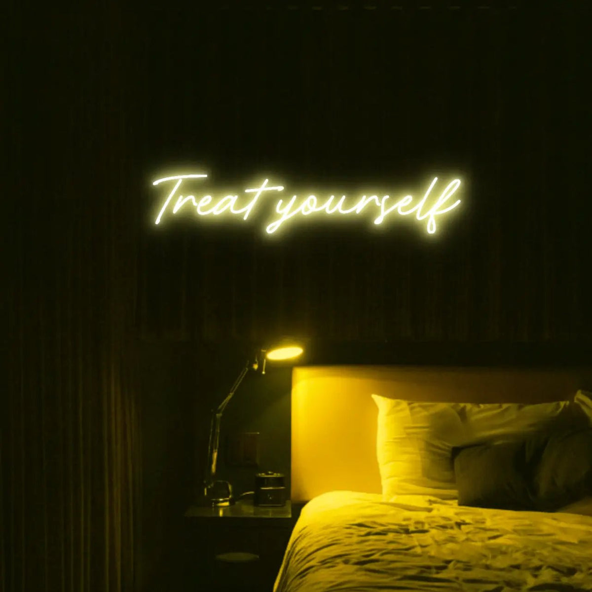 Treat Yourself LED Neon Light Sign in yellow, featuring script lettering illuminated above a bed in a dark bedroom.