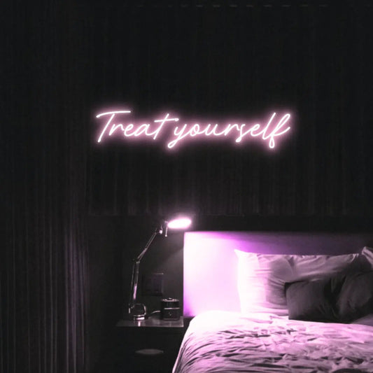 Treat Yourself LED Neon Light Sign in pale pink, featuring script lettering illuminated above a bed in a dark bedroom.