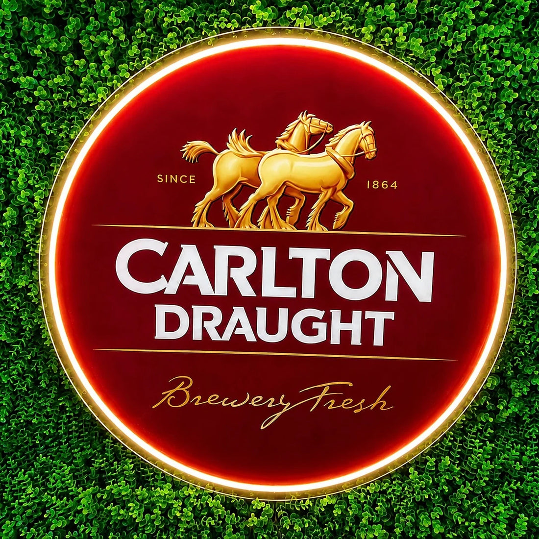 Carlton Draught Neon Sign, featuring illuminated beer-brand logo on a green foliage wall.