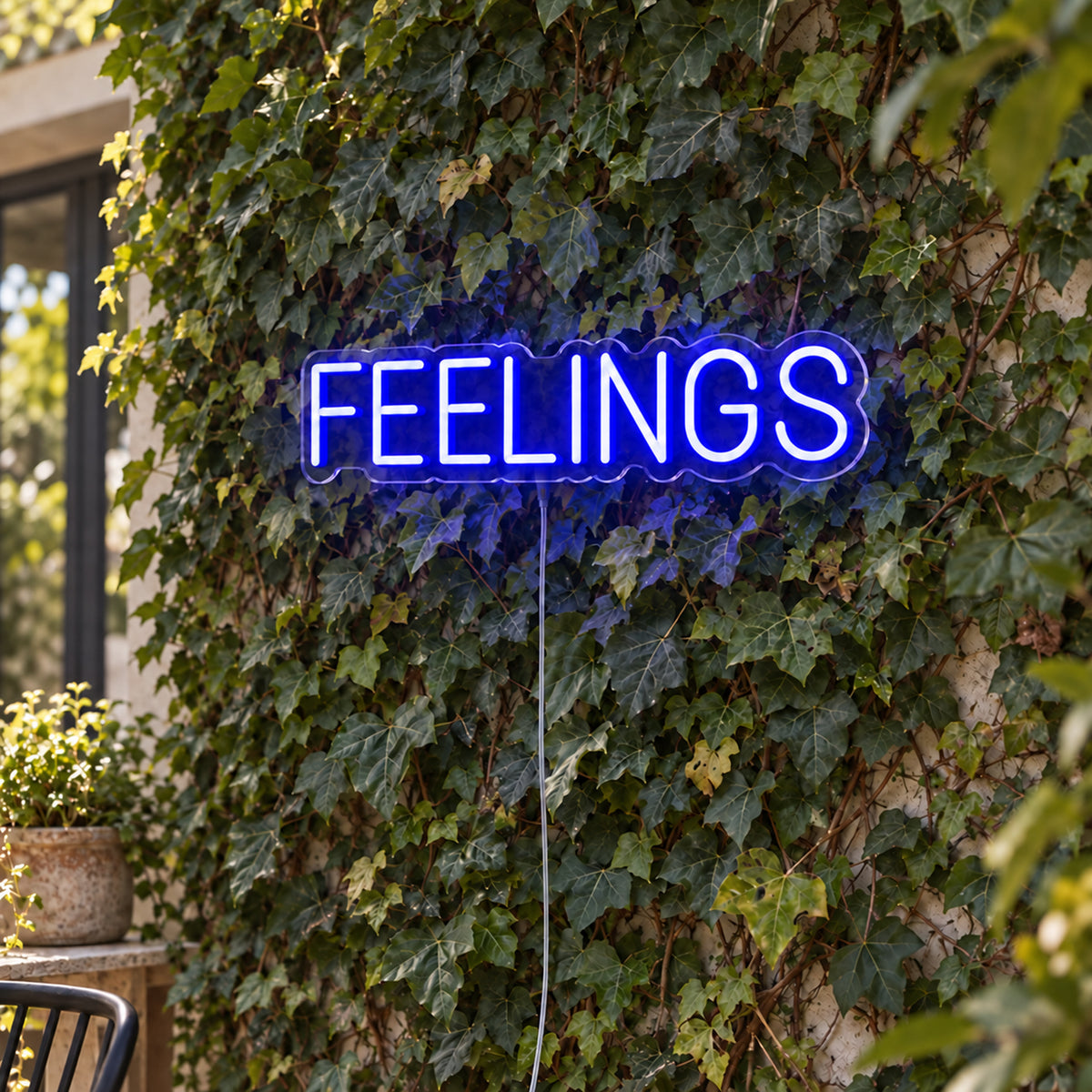 Feelings Neon Sign in blue, featuring block lettering against a foliage wall.
