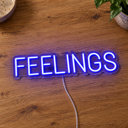 Feelings Neon Sign in blue, featuring block lettering on a wooden surface.