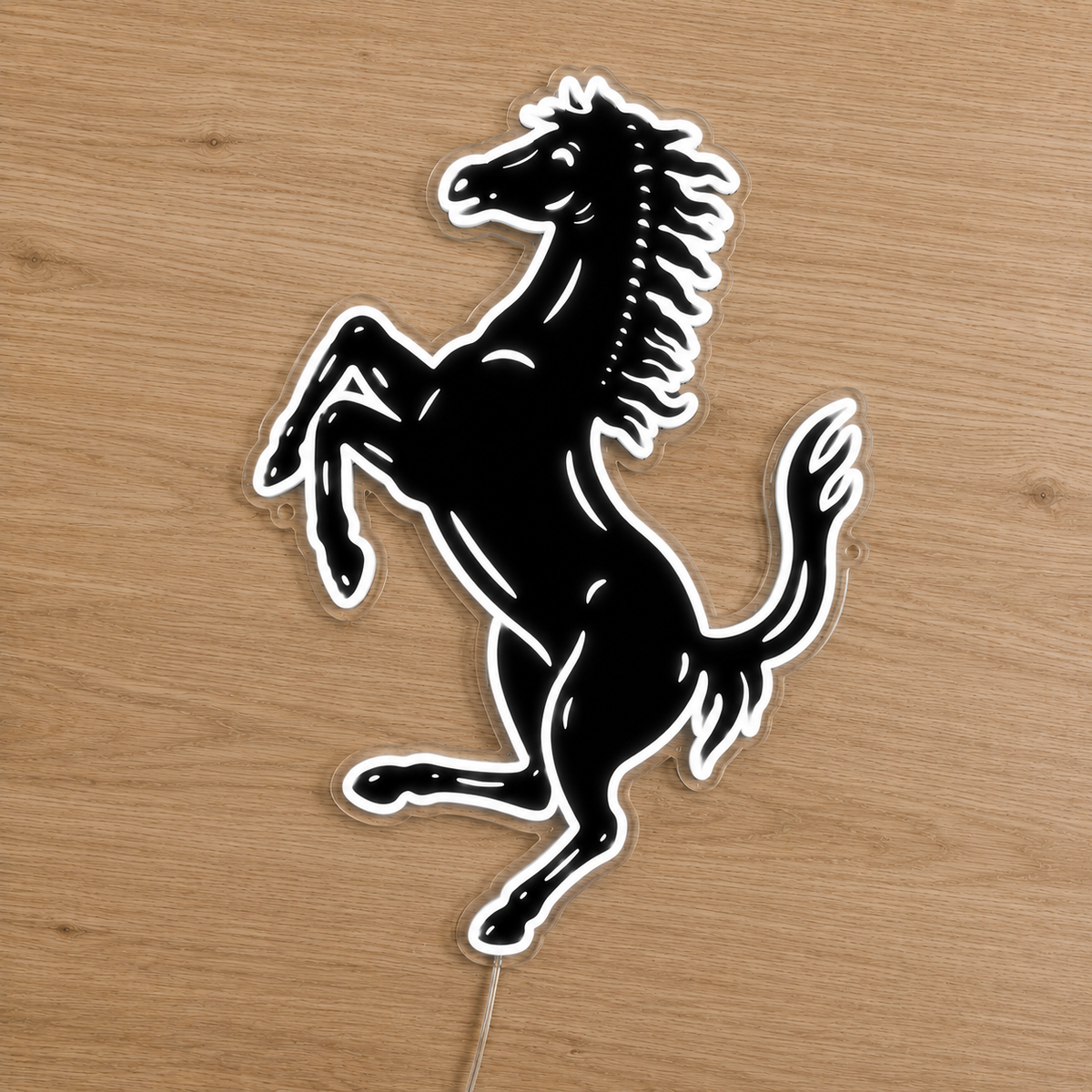 A black and white Ferrari prancing horse decal or sticker displayed on a light brown wooden surface.