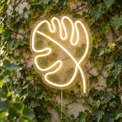 Leaf LED Neon Light Sign in warm white, featuring monstera-leaf outline against a green foliage wall.