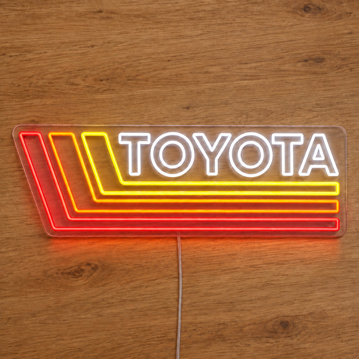 Toyota Retro Land Cruiser LED Neon Sign in white, red and yellow, featuring Toyota lettering with retro stripes on a wooden surface.