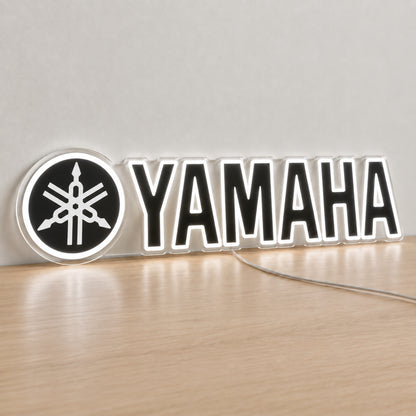 Yamaha (Black) LED Neon Sign in white, featuring Yamaha lettering beside a tuning-fork emblem on a light reflective surface.