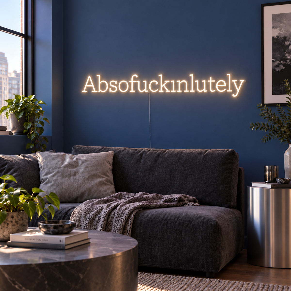 Warm White version of the Absofuckinlutely Neon Sign, shown above a charcoal sofa on a blue wall.