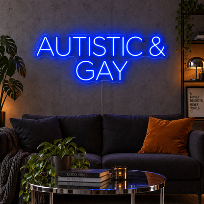 Autistic & Gay Neon Sign glowing blue above a dark sofa against a concrete wall.