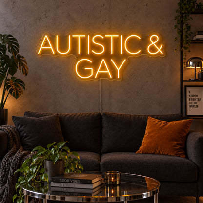 Autistic & Gay Neon Sign glowing gold above a dark sofa against a concrete wall.