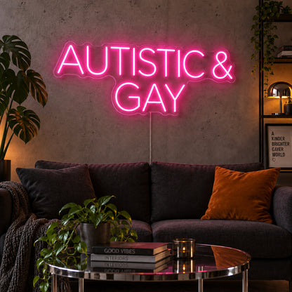 Autistic & Gay Neon Sign glowing pink above a dark sofa against a concrete wall.