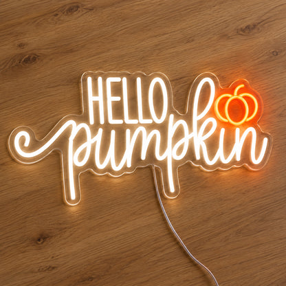 Hello Pumpkin White Neon Sign featuring white Hello Pumpkin lettering with flowing script and a small orange pumpkin, illuminated on clear acrylic lying on a natural oak wooden surface.