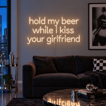Warm White version of the Hold My Beer While I Kiss Your Girlfriend Neon Sign, shown above a burgundy sofa.