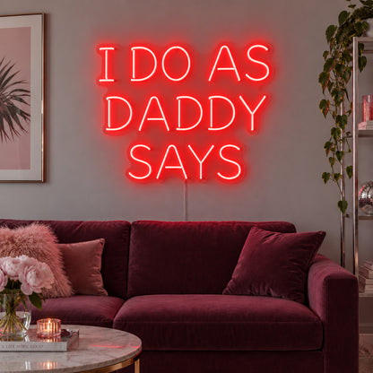 I Do As Daddy Says Neon Sign with red lighting, displayed above a burgundy sofa.
