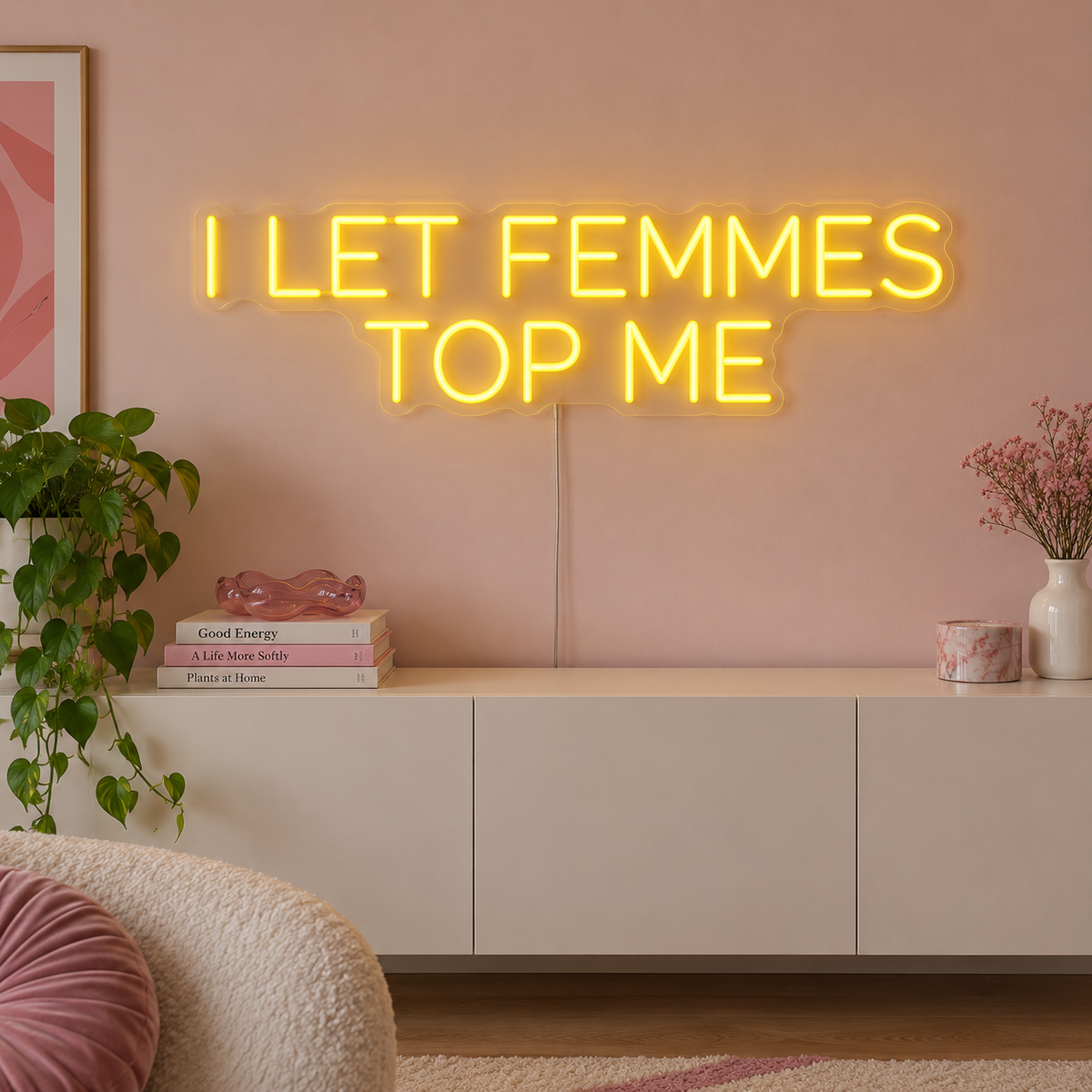 I Let Femmes Top Me Neon Sign in yellow in rounded lettering above a white sideboard.
