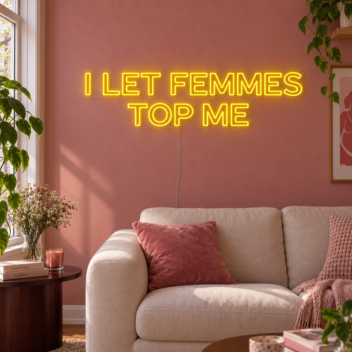 I Let Femmes Top Me Neon Sign in yellow in outlined lettering above a cream chair.