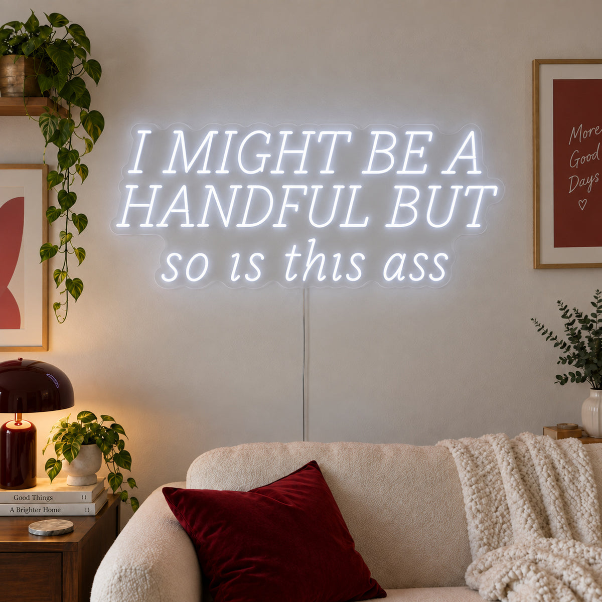 I Might Be A Handful But So Is This Ass Neon Sign, RGB colour-changing option shown in white in wide lettering above a cream sofa.