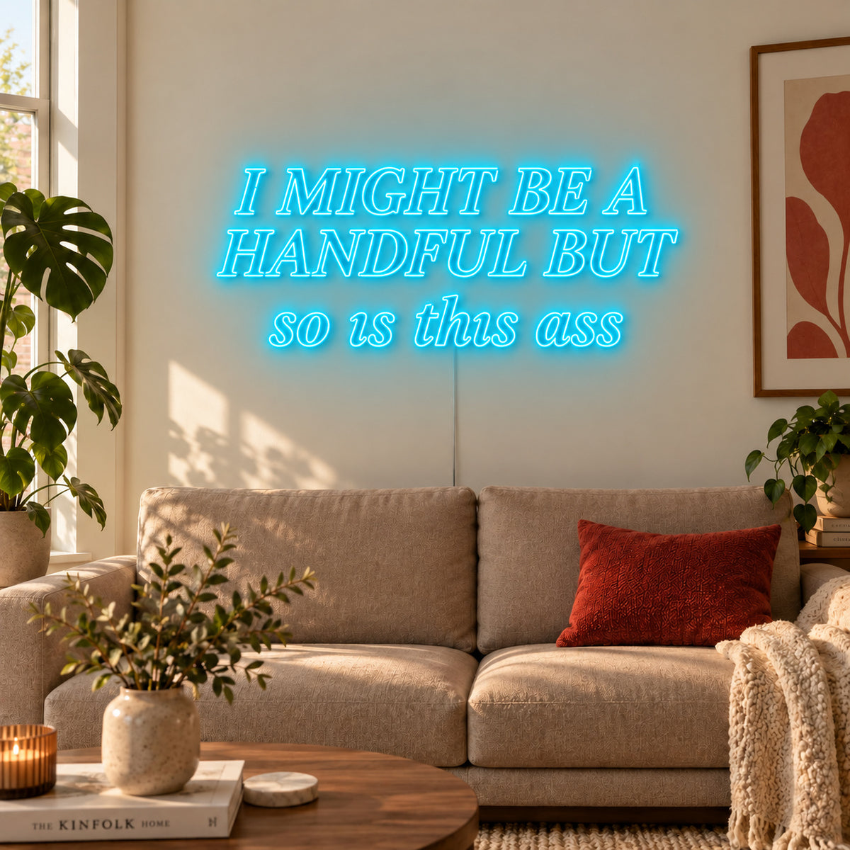 Ice Blue version of the I Might Be A Handful But So Is This Ass Neon Sign, shown in compact lettering above a cream sofa.