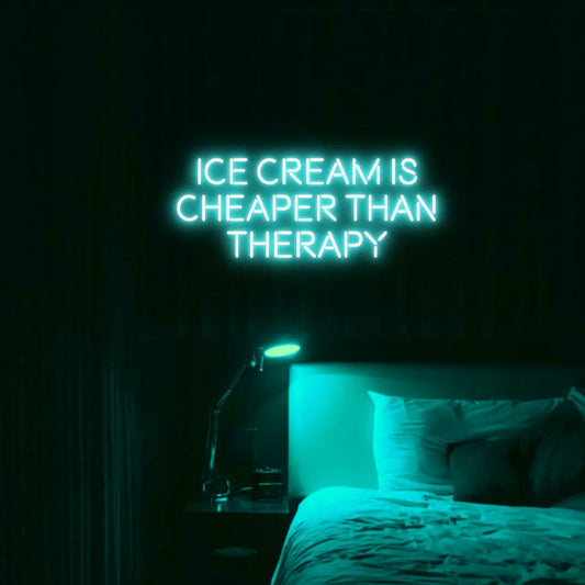Ice Cream Is Cheaper Than Therapy LED Neon Light Sign in turquoise, featuring three lines of block lettering illuminated above a bed.