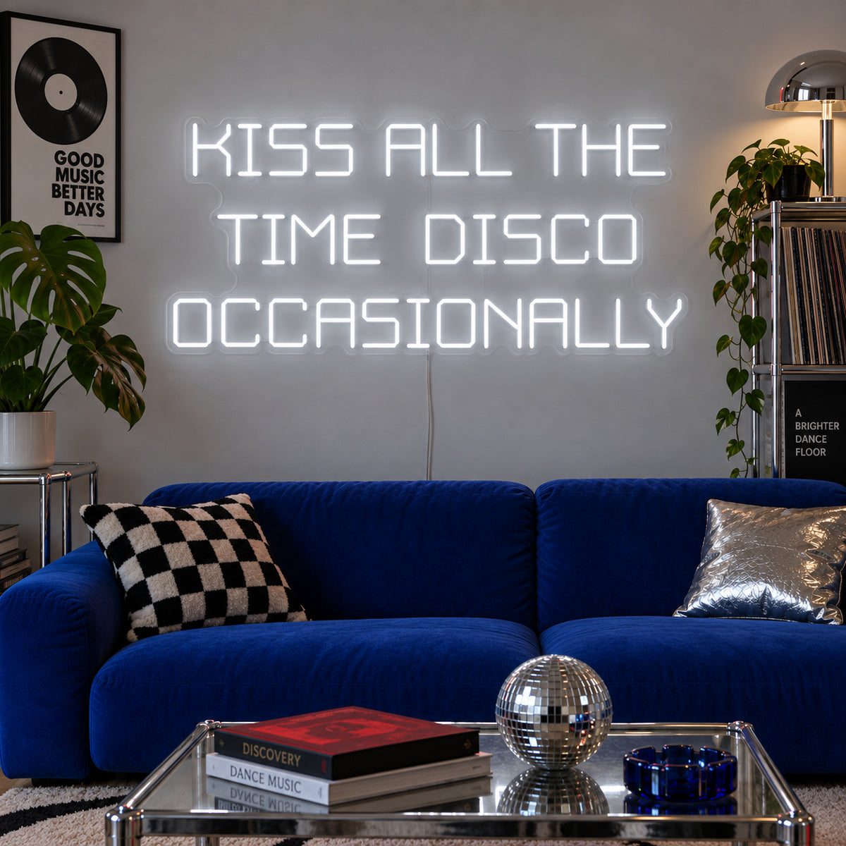 Kiss All The Time Disco Occasionally Neon Sign glowing white above a blue sofa near a disco ball.