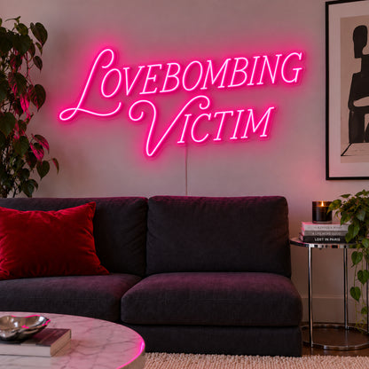 Rose Red version of the Lovebombing Victim Neon Sign, shown above a dark sofa with red cushions.