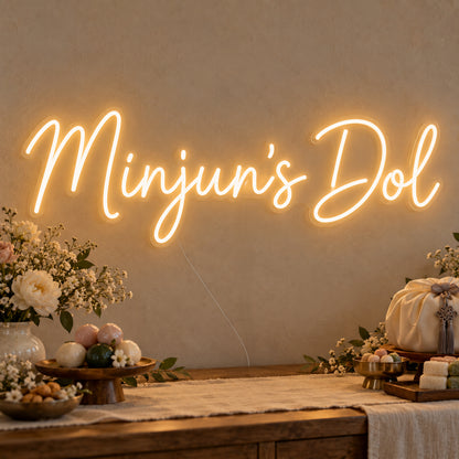 Personalised Dol Neon Sign on clear cut-to-shape acrylic, illuminated on a wall in a styled celebration setting; sample personalised wording shown